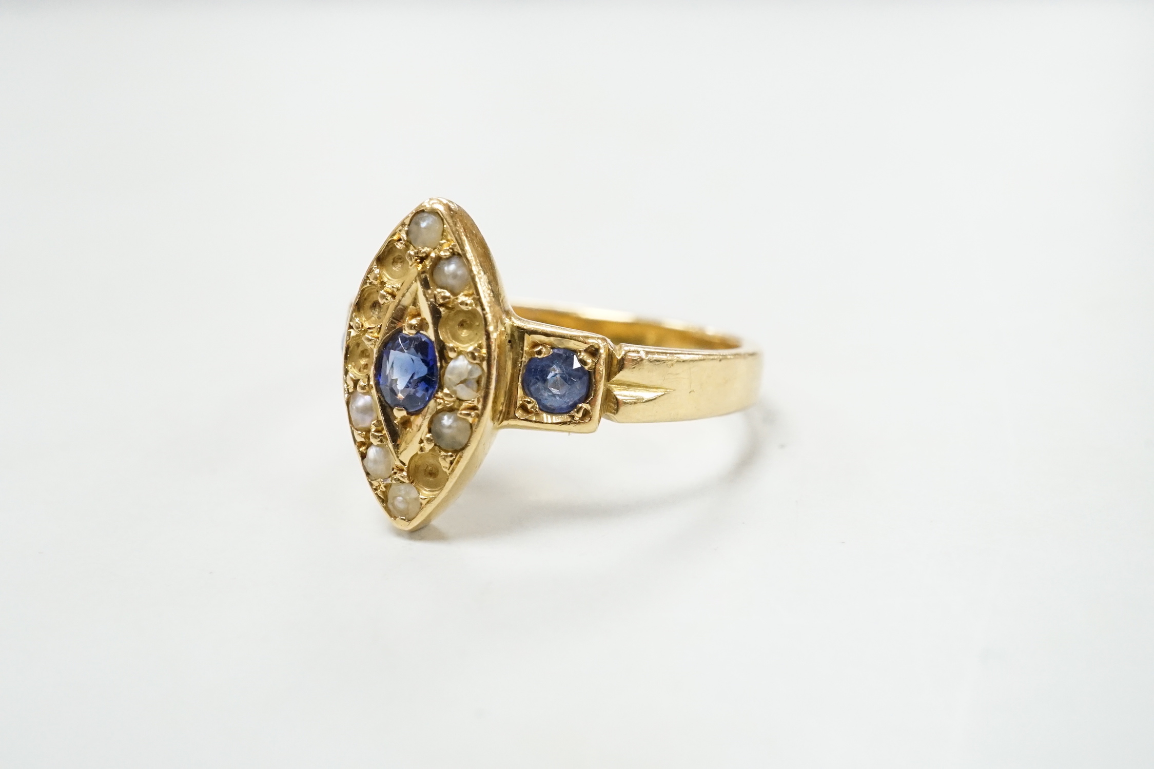 An early 20th century yellow metal, sapphire and seed pearl set marquise cluster ring (pearls missing), size L/M, gross weight 3.6 grams.